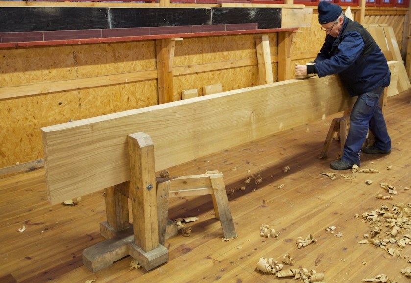 Tomas Karlsson høvlar kant på benkeplate til høvelbenk. Emnet er 3,8 meter langt, 15" bredt og 3 1/2" tjukt. For å få emnet fast på kant spente vi det opp i to lause bukkar til ein skottbenk. Foto: Roald Renmælmo