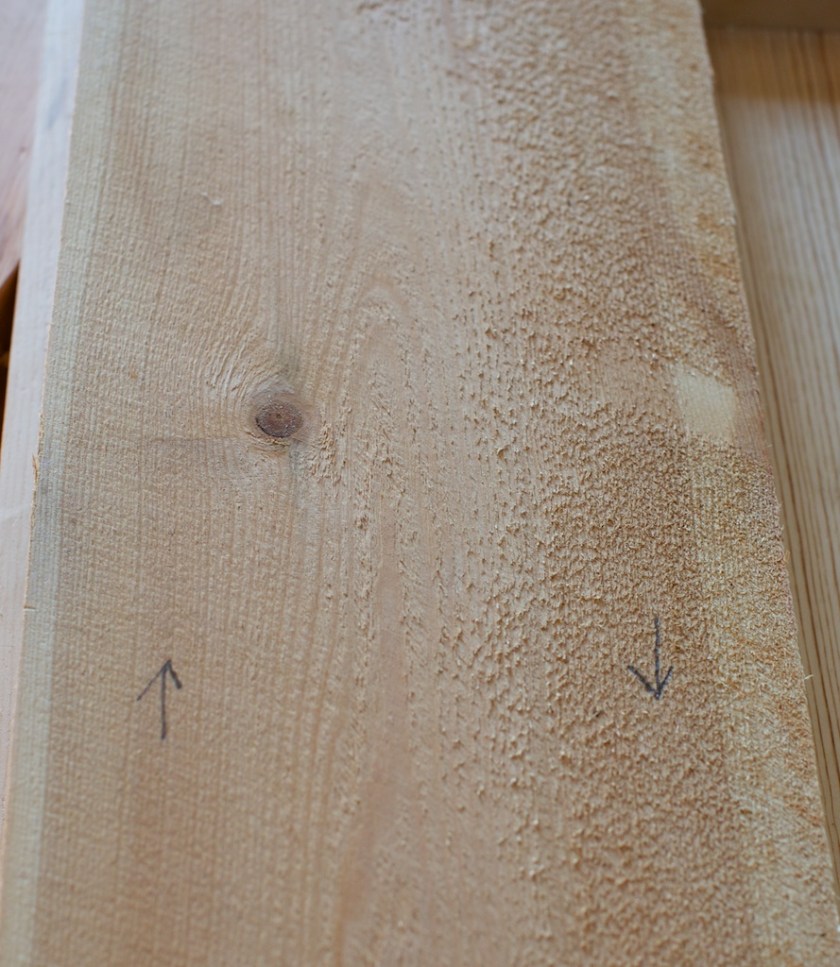 Bord som er saga av tømmer som er vindt, altså høgrevridd, vil få motved på høgre side og medved på venstre side. Her er det markert med piler med blyant. Når eg høvlar slike bord ser eg med eint gong på strukturen i overflata på bordet at veden går mot den retninga eg høvlar. Biletet er tatt med baklys frå vindauget og då vert det skygge av  fibrane som står opp i høgre side av bordet. Venstre side ser glattare ut. Foto: Roald Renmælmo